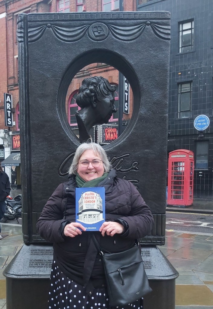 Tina standing by the Agatha Christie Memorial holding a copy of her book Agatha Christie's London